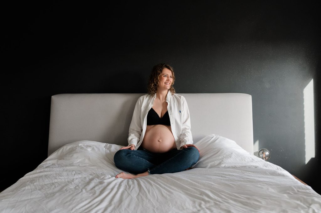 Zwangere vrouw lachend op haar bed.