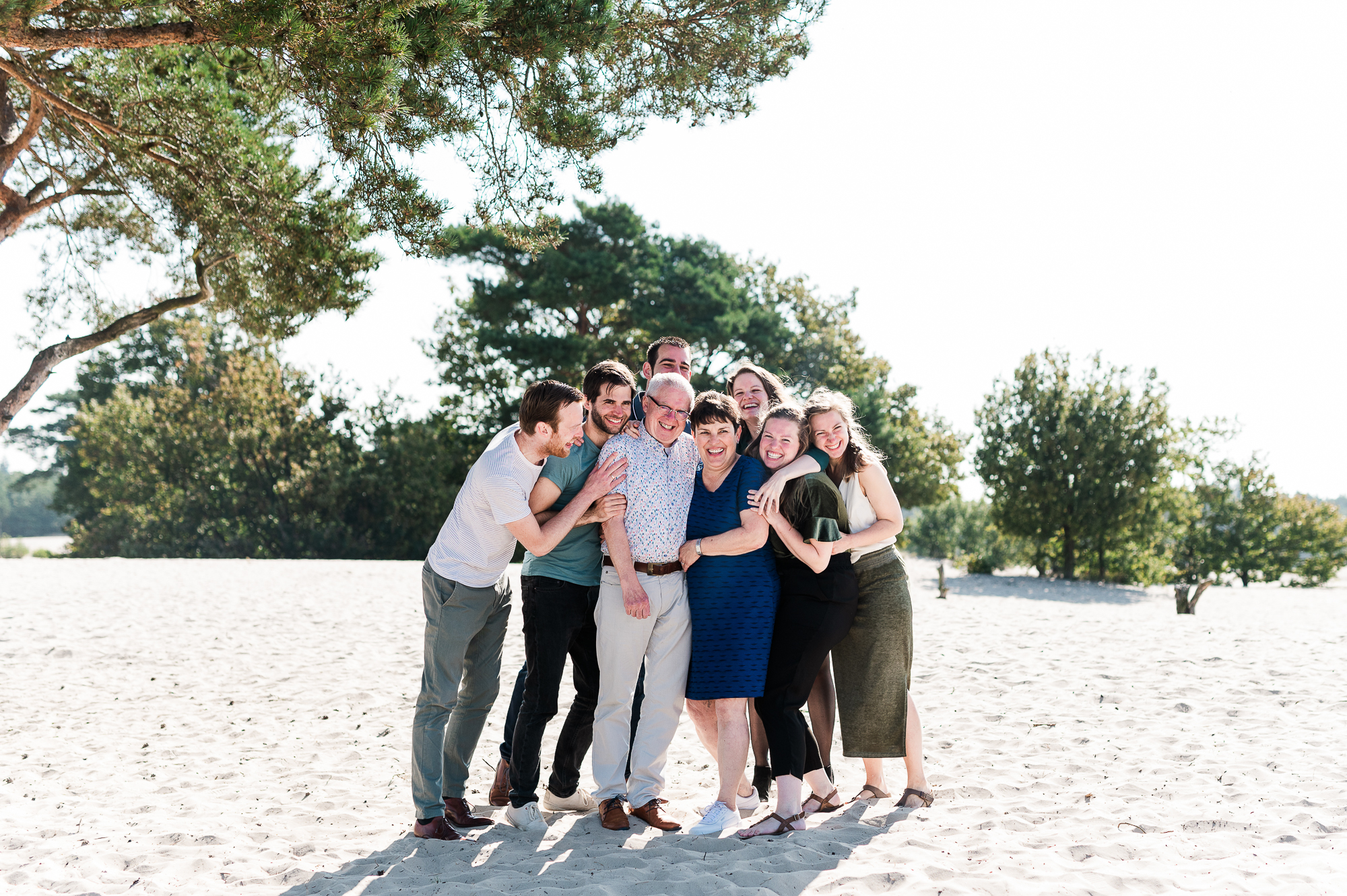 Familie foto met 10 mensen die elkaar innig knuffelen en plezier hebben.