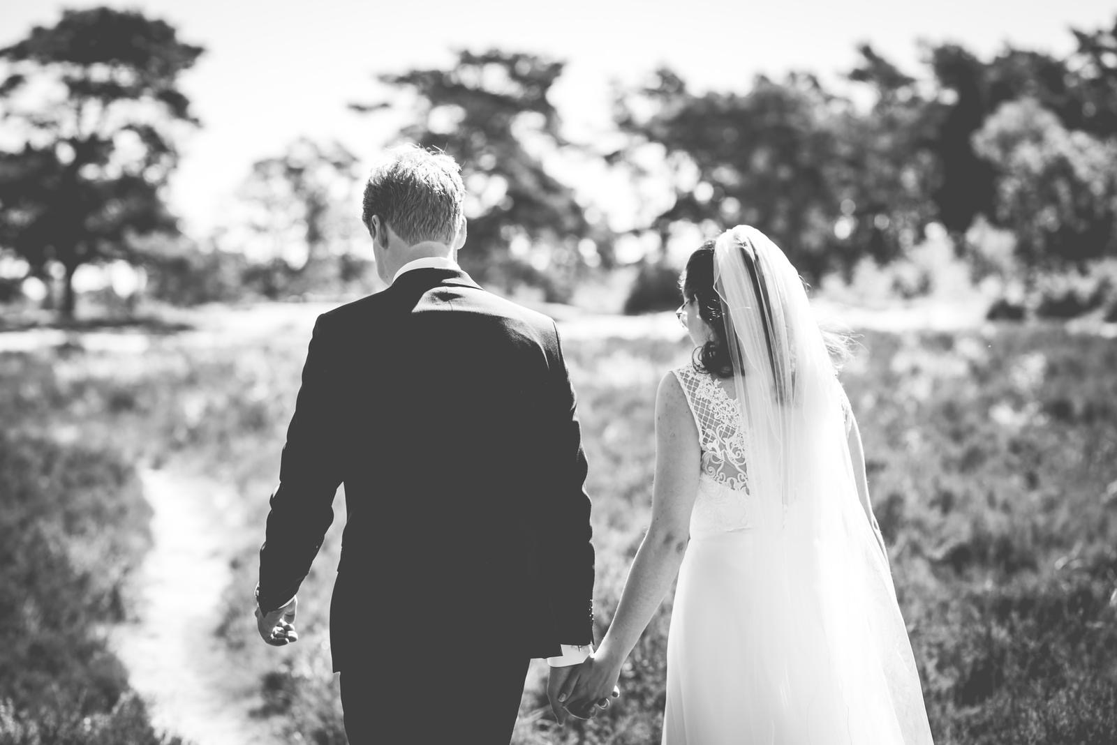 Bruidspaar loopt hand in hand door een Fries landschap tijdens hun bruiloft.