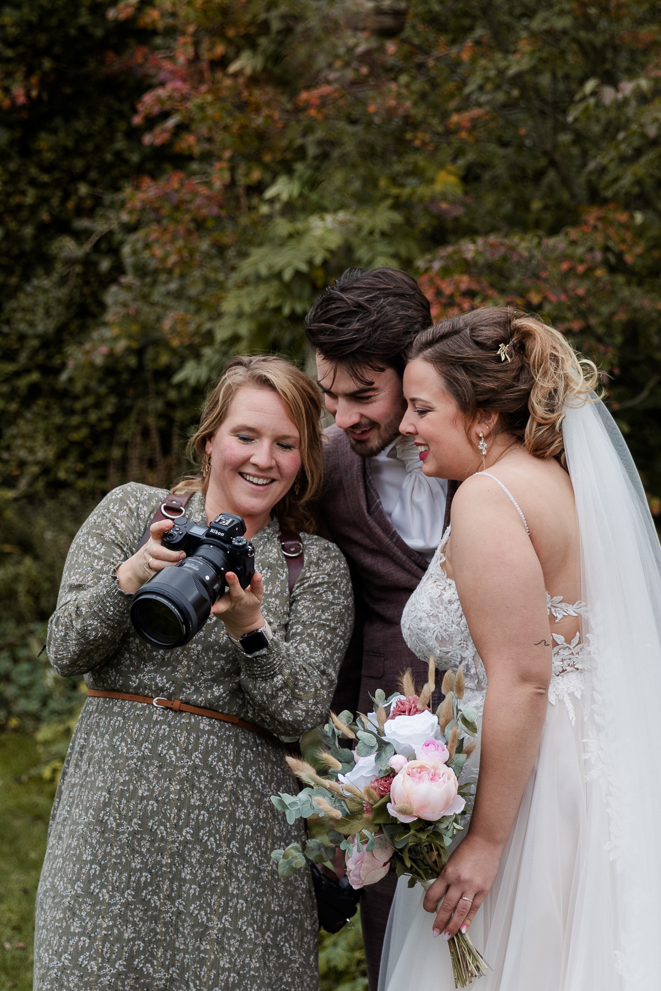 Bruidsfotograaf laat lachend het resultaat van een foto zien aan een bruidspaar.