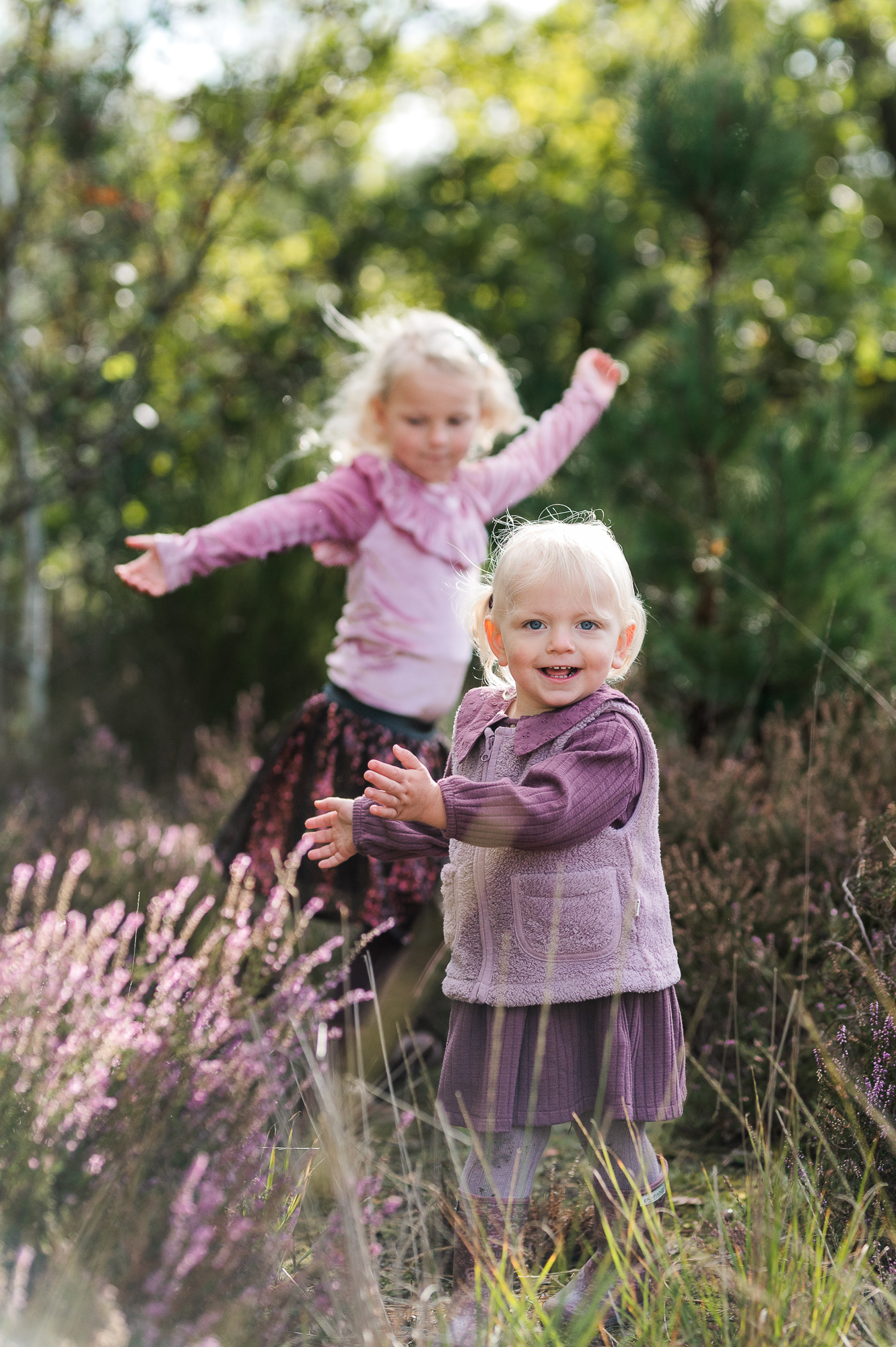 Twee zusjes in paars gekleed die lachend spelen in de natuur.
