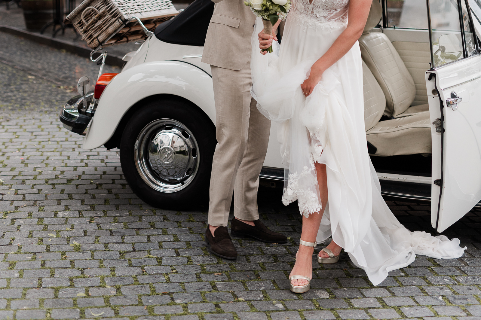 Bruidegom die zijn bruid helpt om uit de auto te stappen, de bruid houdt haar trouwjurk boven de grond. In centrum Breda met hun trouwfotograaf.