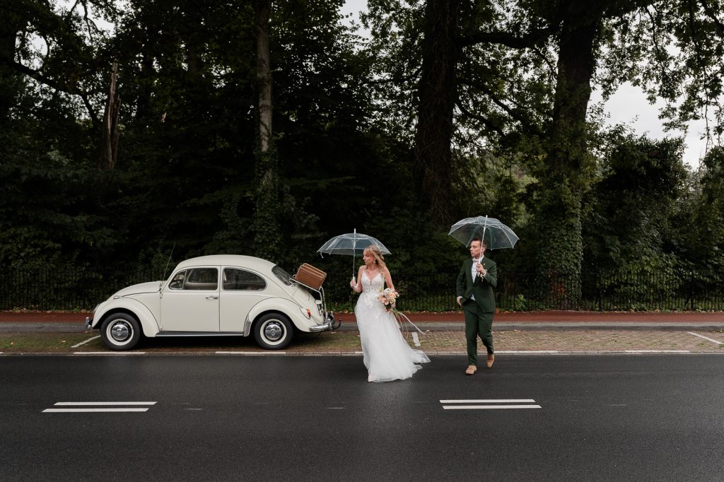 Bruidspaar steekt de weg over met hun paraplu's op hun trouwdag.