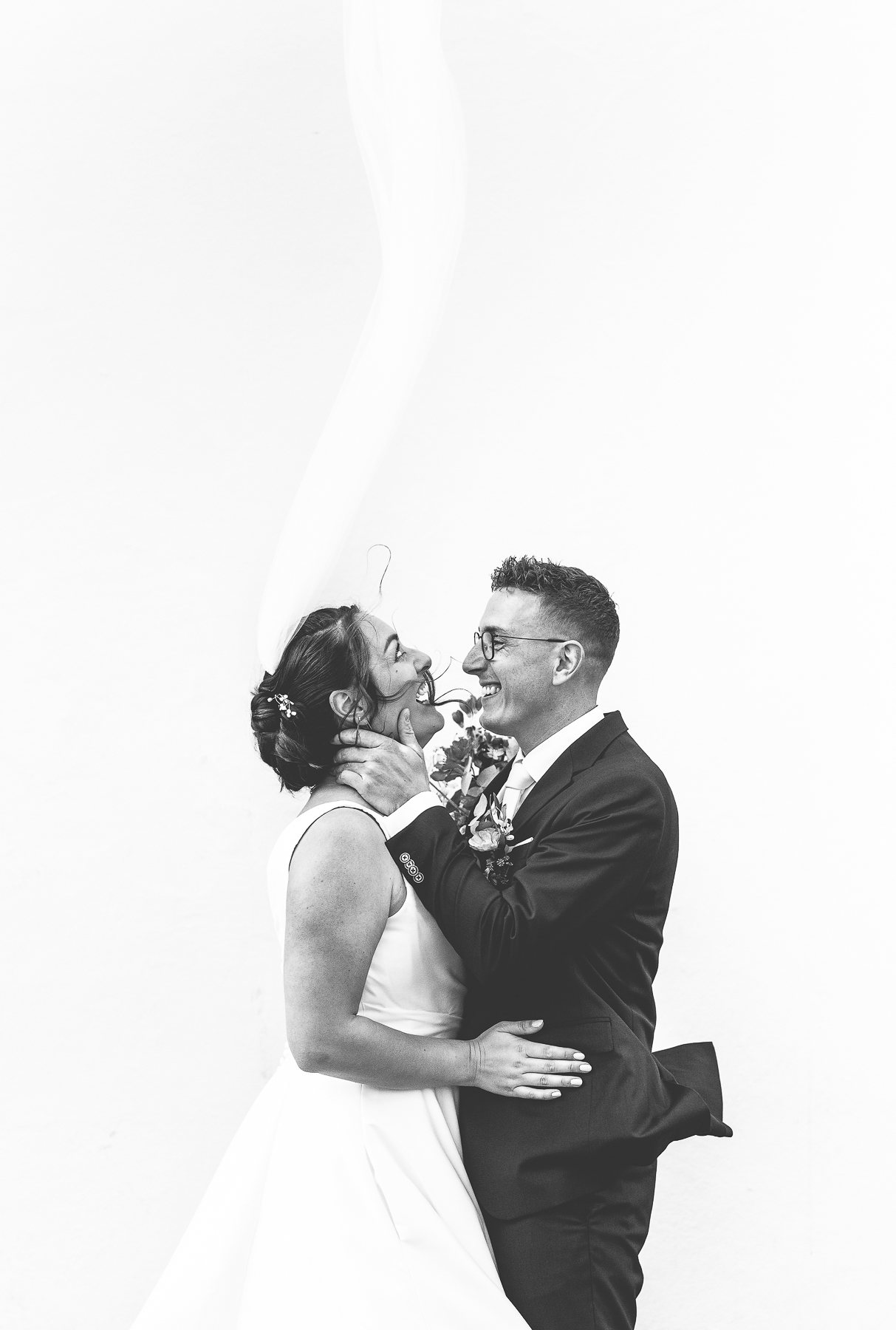 Bruidspaar in centrum van Breda tijdens hun trouw reportage, ze lachen omdat de sluier de lucht in vliegt.